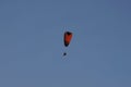 Orange black paraglider with fan in blue sky