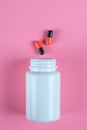 Orange and black pills, tablets and white bottle on pink background Royalty Free Stock Photo