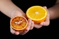 Orange and blood or red orange fruit halves in hands on black background Royalty Free Stock Photo