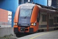 The orange and blue electric train at the railway station. Track, poles and supports for current-carrying lines Royalty Free Stock Photo