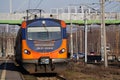 The orange and blue electric train at the railway station. Track, poles and supports for current-carrying lines Royalty Free Stock Photo