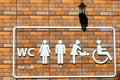 On the orange brick wall is a toilet signpost with white images of a man, a woman, a baby changing scene of a baby