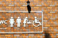 On the orange brick wall is a toilet signpost with white images of a man, a woman, a baby changing scene of a baby