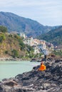 Orange Buddhist monk sitting on riverbank at Rishikesh, holy town and travel destination in India, famous for yoga classes. Clear