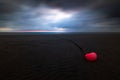 Orange buoy at the beach of Amrum island Germany during low tide with glowing dramatic sky and dark stormy clouds at sunset