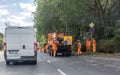 Orange car and brigade road repair workers in orange suits on the highway. Asphalt road workers repairs road