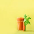 Orange carrot juice with carrots, celery on yellow background. Square crop. Fresh vegetable smothie in glass. Copy space