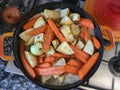 Orange casserole with meat, diced potatoes, carrots and celeriac on gas stove. Onion studded with cloves. Cooking scenery for