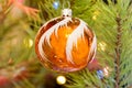 Orange Christmas balloon on a Christmas tree against the background of shining garlands. Orange ball surrounded by branches of the Royalty Free Stock Photo