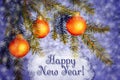 Orange Christmas ornaments on spruce branches on a blue shiny background with snowflakes. Lettering Happy New Year on a Royalty Free Stock Photo