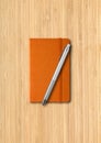 Orange closed notebook with a pen on wooden background