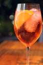 Orange cocktail with orange garnish in wine glass, aperol spritz in sunny setting