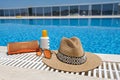 Orange coloured beach accessories near swimming pool. Sun cream, sunglasses, music speaker and straw hat