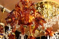 Orange coloured decorative crystal chandelier with floral motives surrounded by other crystal chandeliers