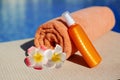 Orange cotton towel and sunscreen body lotion in a orange tube on the background pool. Means for skin care, concept