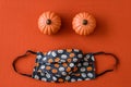 Orange and cream colored pumpkin patterned fabric face mask, with two ceramic pumpkins, on an orange background Royalty Free Stock Photo