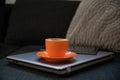 Orange cup of coffe and digital tablet placed on laptop computer sitting on a couch