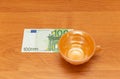 Orange cup without a saucer, 100 euro, golden background, orange table. Empty cup. The focus on the euro. Royalty Free Stock Photo