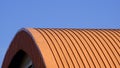 Orange curved corrugated steel roof against blue clear sky background Royalty Free Stock Photo