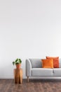 Orange cushions on grey settee next to plant on wooden table. Real photo