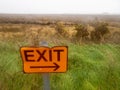 Orange and dark sign exit by a green field. Light and airy mood and feel. Direction signpost