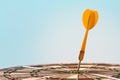 Orange dart arrow hitting bulls-eye in center of dartboard on blue sky background Royalty Free Stock Photo