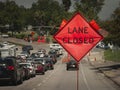 An orange diamond shaped roadwork sign stating lane closed with traffic backed up in the distance