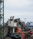 an orange digger with a backhoe working on a large urban demolition site with a metal tower crane at the edge of the frame and