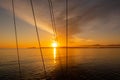 Orange dramatic sunrise over the sea with bank of dark clouds on the sky seen through the shrouds and ropes on a sailing boat