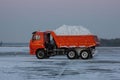 Orange dump truck rides on a winter road with snow in the back