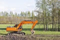 Orange excavator on the background of a meadow and trees