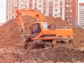 An orange excavator on a construction site against the background of a multi-storey building digs a trench. Royalty Free Stock Photo