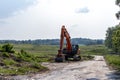 Orange excavator on dirt road - rural scenery with grassy field and trees Royalty Free Stock Photo