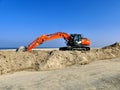 Orange excavator on pile of sand near beach Royalty Free Stock Photo