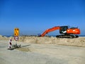 Orange excavator on pile of sand with road signs on construction