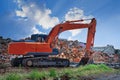 An orange excavator stands against the backdrop of a destroyed building and a blue sky Royalty Free Stock Photo