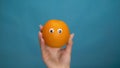 Orange with eyes in a woman hand on a blue background. Woman hand close-up. Royalty Free Stock Photo