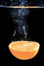 An orange falling into water on a black shiny background falls under water with bubbles Royalty Free Stock Photo