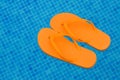 Orange flip flops floating in blue pool water