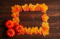 Orange frame made from bright fall leaves and pumpkins on the brown wooden background