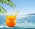 Orange fruit as the cup with orange juice splash and straw. Blue sparkling sea at the background. Drink concept Royalty Free Stock Photo