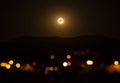 Orange full moon rising over the village mountain.