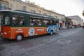 An orange and green trolley bus from Old Town Trolley driving on River Street with shops and restaurants and people walking