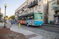 An orange and green trolley bus from Old Town Trolley driving on River Street with shops and restaurants and people walking