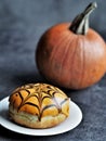 Orange halloween donut with spider web on plate and pumpkin on dark background