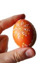 Orange hand painted easter egg with yellow flowers, held in left hand of adult male person, white background.