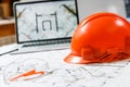 Orange hard hat, laptop with drawings and protective glasses with blueprints on a table
