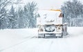 Orange highway maintenance gritter plough truck completely covered with snow, cleaning forest road, view from car Royalty Free Stock Photo