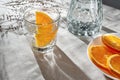 Orange infused water in glass, bottle, sliced oranges on beige table with aesthetic sunlight shadows, lifestyle healthy drink, Royalty Free Stock Photo