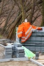 The orange jacket of a builder lies on a pile of paving slabs against the backdrop of growing trees in the park. Vertical image